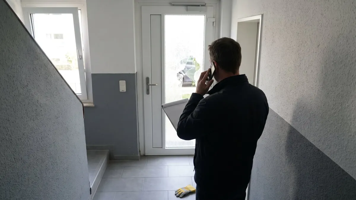 Bewohner telefoniert und sieht dabei auf die beschädigte Glastür im Hausflur